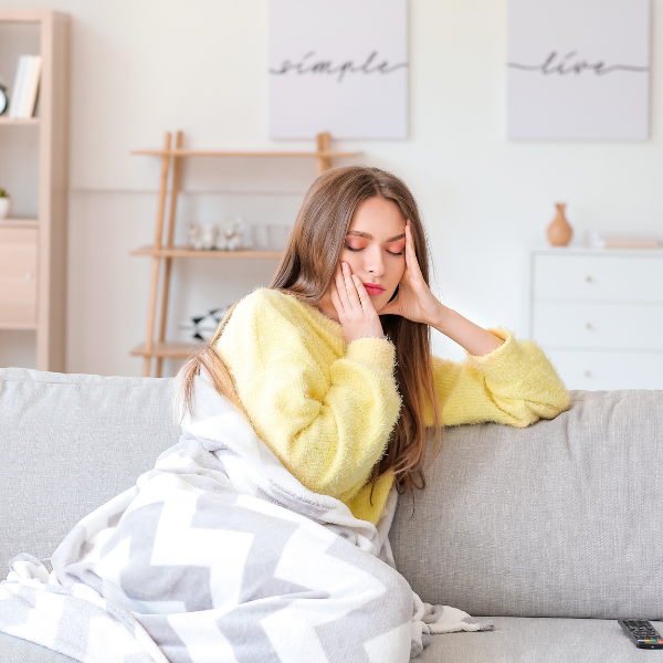 Woman sitting on coach looking ill with blanket on, early pregnancy