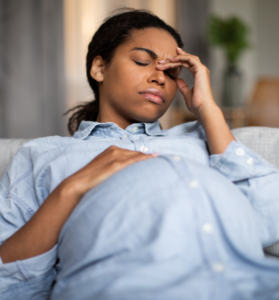 BIPOC woman pregnant eyes closed head in her hands, exhausted, sick, hyperemesis gravidarum